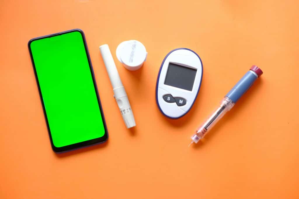 Söt frukt, bättre blodsockerkontroll? Så hänger mango och blodsocker ihop vid prediabetes 2 Blodsockermätare, insulinpenna och mobil på orange bakgrund – mango och blodsocker kopplat till prediabetes.