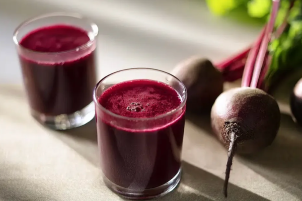 Vad är rödbetsjuice bra för? Två shots med rödbetsjuice står på ett bord bredvid några rödbetor.