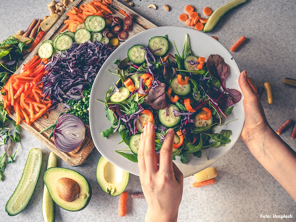 Hand håller skål med sallad av kål, gurka och morot – nordisk kost, medelhavsinspirerad, kopplad till bättre blodsockerkontroll vid typ 2-diabetes och mindre fettlever.