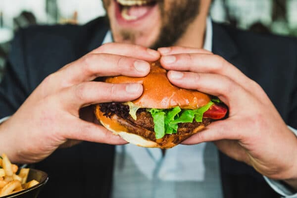 Person som äter hamburgare – blodsocker efter måltid kan påverka blodsockernivåer och ge hög blodsockernivå, vilket kopplas till Alzheimer i ny studie om blodsockervärde.