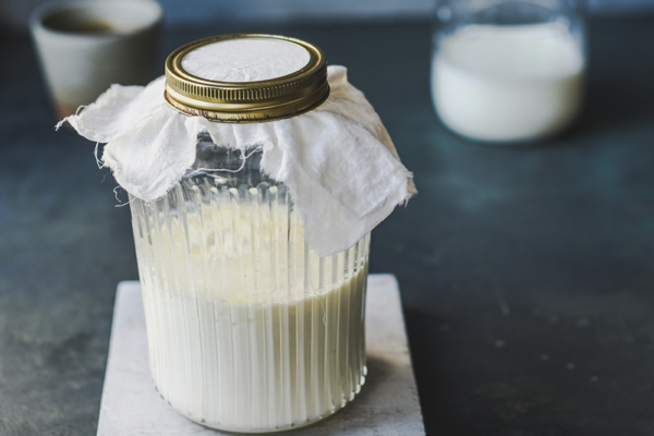 Glasburk med fermenterad kefir under tyglock på köksbänk – är kefir nyttigt?