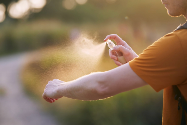 Bästa myggmedlet 2026 – person sprayar myggmedel på armen utomhus i kvällsljus