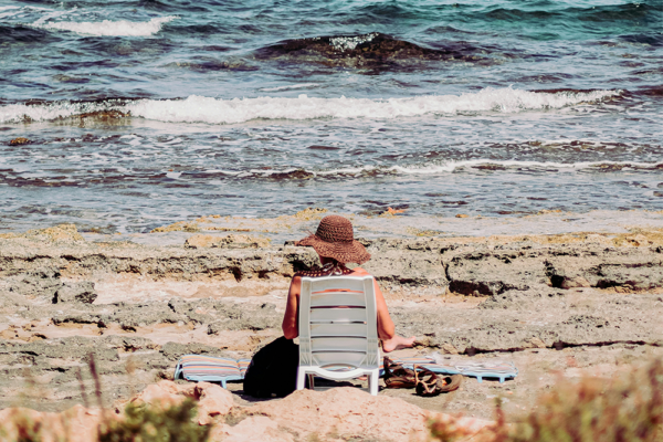 Bästa solkrämen för stranden – kvinna sitter vid havet och njuter av solen