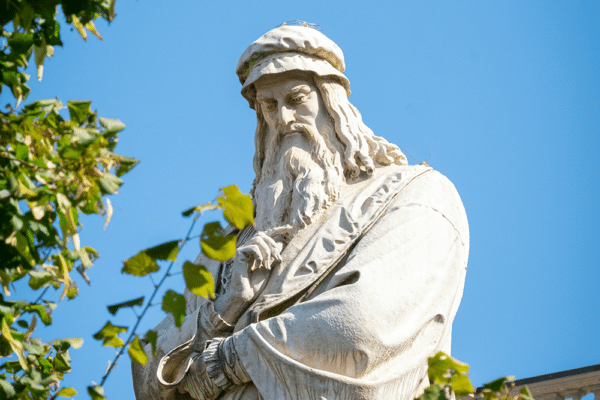 Vit Leonardo da Vinci-staty, blå himmel och gröna löv.