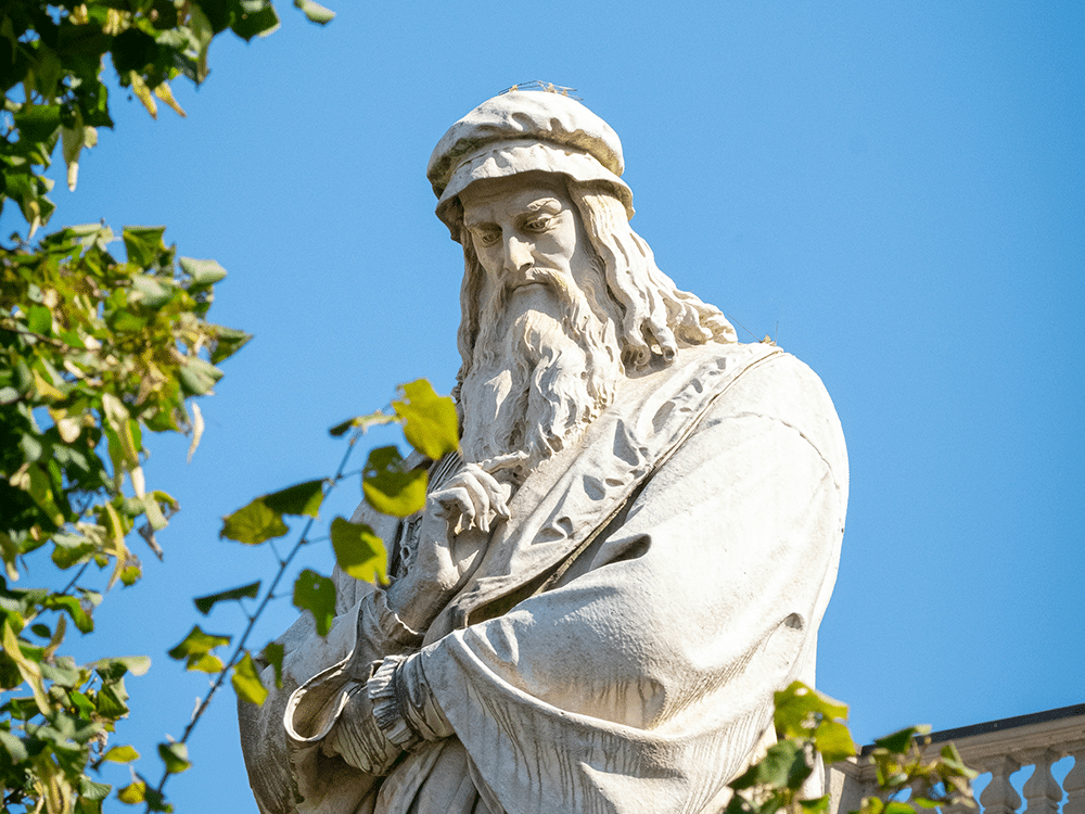 Vit Leonardo da Vinci-staty, blå himmel och gröna löv.
