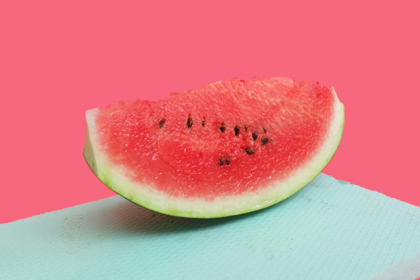 Saftig skiva vattenmelon med kärnor på färgglad rosa och turkos bakgrund för en artikel om vattenmeloner och hälsa.