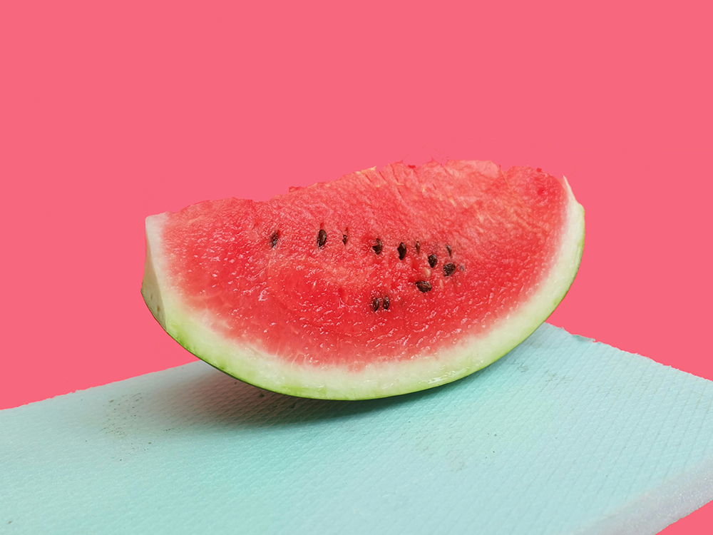 Saftig skiva vattenmelon med kärnor på färgglad rosa och turkos bakgrund för en artikel om vattenmeloner och hälsa.