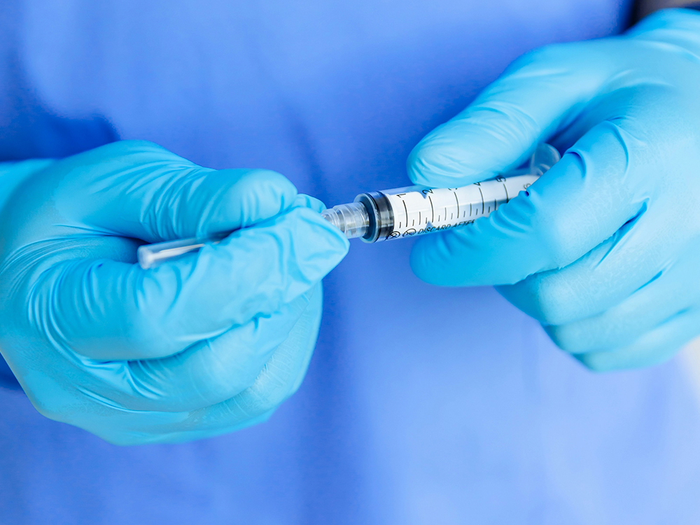 Vårdpersonal med blå handskar förbereder en spruta med bältrosvaccin.