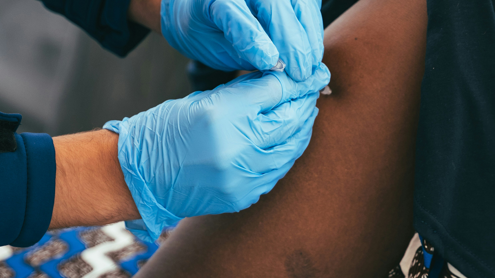 En person får bältrosvaccin i överarmen av vårdpersonal med blå handskar.