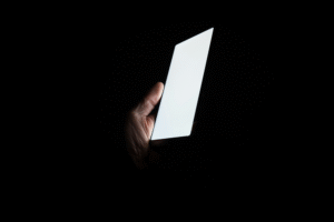 Hand som håller i en mobiltelefon i mörker – ljusexponering på kvällen kan störa dygnsrytm och sömn