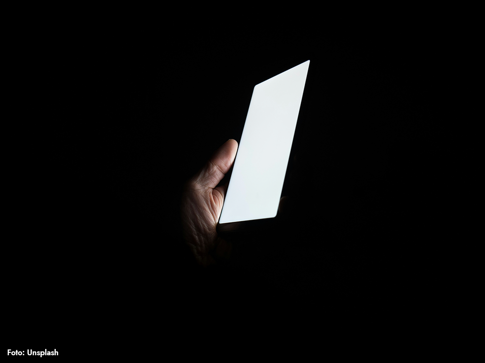 Hand som håller i en mobiltelefon i mörker – ljusexponering på kvällen kan störa dygnsrytm och sömn