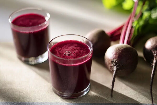 Vad är rödbetsjuice bra för? Två shots med rödbetsjuice står på ett bord bredvid några rödbetor.