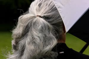 Varför blir håret grått – person med gråa hår i hästsvans, under svartvitt paraply, sedd bakifrån utomhus.