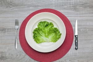 Kalorirestriktion förlänger livet – symbolisk bild av liten portion sallad på stor tallrik som illustrerar kalorirestriktion, att försöka förlänga livet och åldras långsammare.