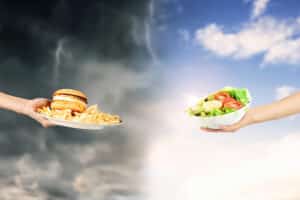 Illustration om ultraprocessad mat där en hand räcker fram hamburgare och pommes frites mot mörk himmel som exempel på ultraprocessad mat, och en annan hand räcker fram sallad som symbol för medelhavskost/medelhavsdiet – ett visuellt svar på frågan: vad är ultraprocessad mat?