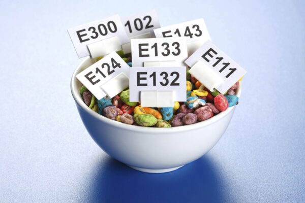Emulgeringsmedel och andra E-nummer i maten: skål med flingor och skyltar med E-nummer som illustrerar hur tillsatser kan påverka tarmfloran och tarmmiljön.