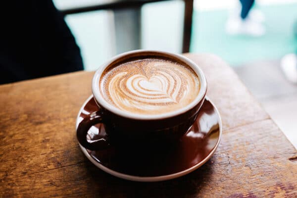 En kopp kaffe med hjärtformat latte art-mönster på ett träbord – illustrerar kaffe och hälsa samt måttlig kaffekonsumtion och hälsa.