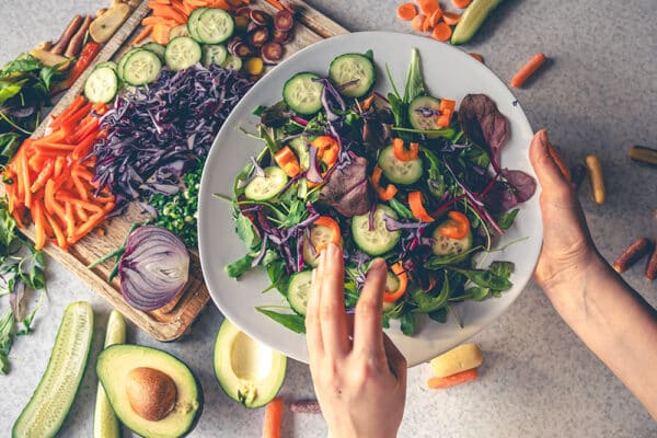 Hand håller skål med sallad av kål, gurka och morot – nordisk kost, medelhavsinspirerad, kopplad till bättre blodsockerkontroll vid typ 2-diabetes och mindre fettlever.